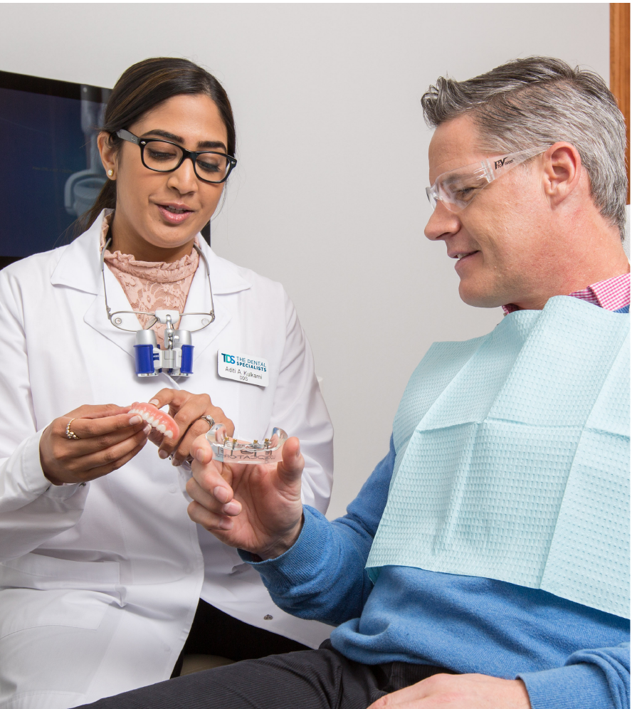 A female dental provider explains a dental implant to a middle-age male patient.